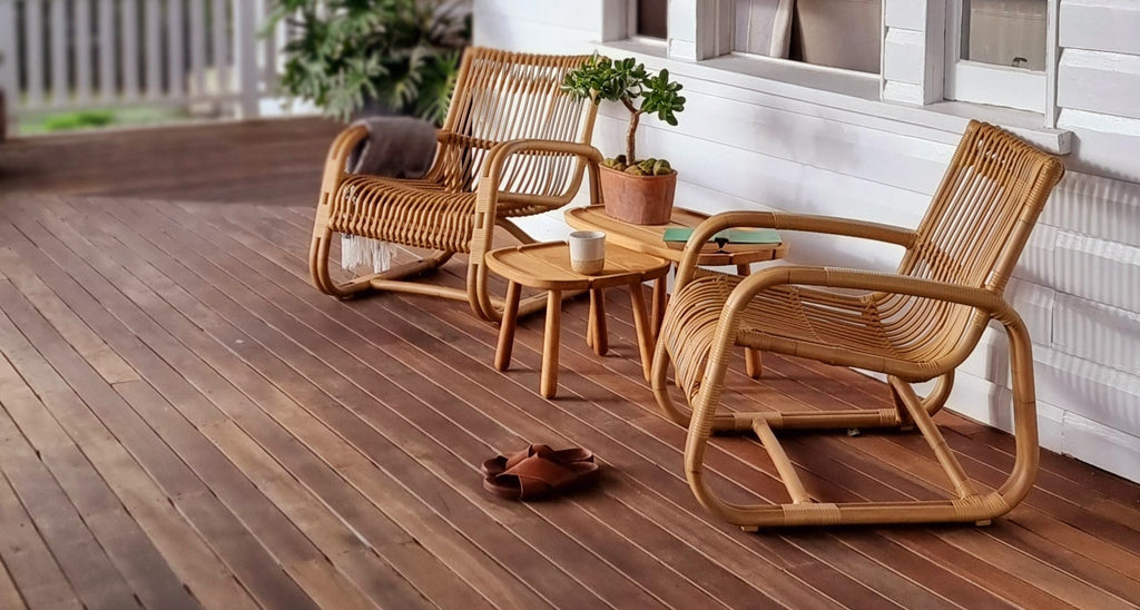 Two sculptural lounge chairs in natural on a veranda with small side tables in teak