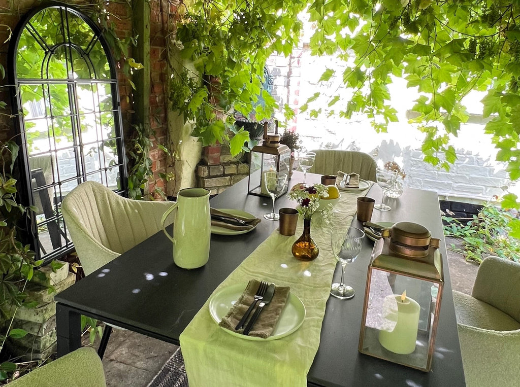 Green pergola with grapevines in the summer time, with a cozy dining setting with soft sand bouclé chairs and black outdoor dining table