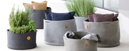 Collection of woven storage baskets featuring decorative cushions and greenery, arranged for a stylish display.