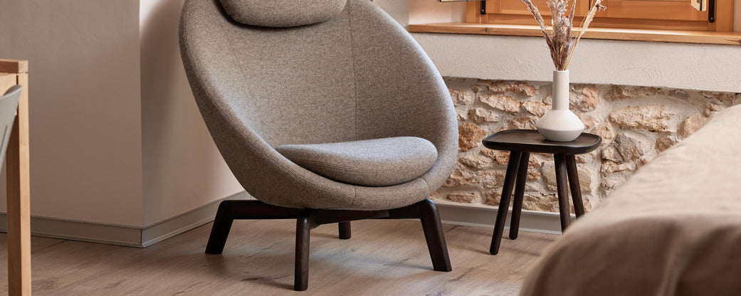 A cozy, modern armchair complemented by a sleek side table, accented with a vase and decorative elements against a textured wall.