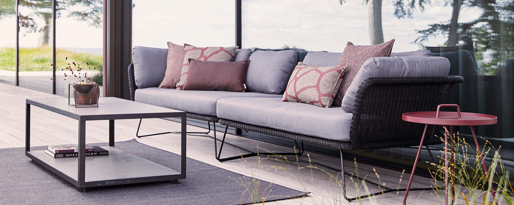 Modern sectional sofa with decorative pillows and a minimalist coffee table, set against a natural backdrop, creating a stylish relaxation area.