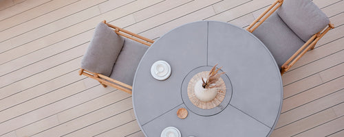 Round dining table with soft seating, complemented by decorative plates and a centerpiece arrangement. Simple, elegant design.