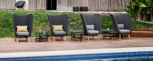 A row of stylish highback chairs with cushions and small tables, positioned near a poolside area.