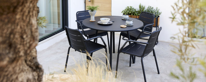 A stylish black table surrounded by four matching chairs, set with dishes and decorative items, evoking a modern dining atmosphere.