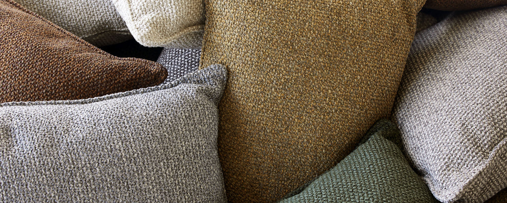 A collection of textured scatter cushions in various earthy tones, piled together for a cozy aesthetic.
