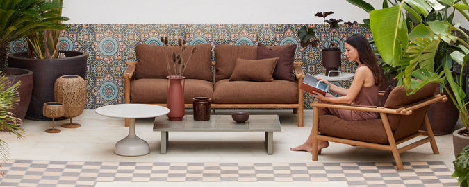 A cozy seating area featuring brown lounge chairs, a coffee table, plants, and decorative wall tiles, creating a relaxed ambiance.