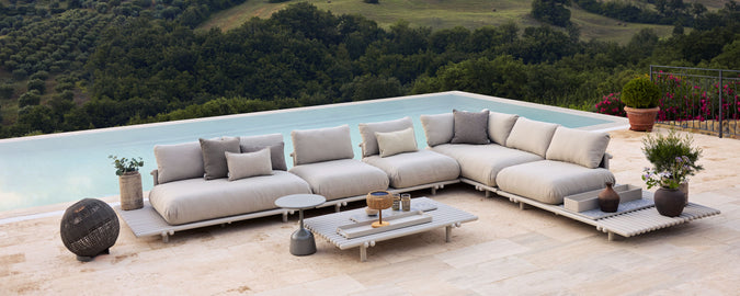A stylish arrangement of modular sofas with cushions, accompanied by a coffee table and plants, set against a scenic nature backdrop.