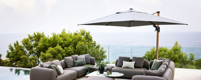 Stylish outdoor seating area featuring a large parasol providing shade beside a serene pool and lush greenery. Perfect for relaxation.