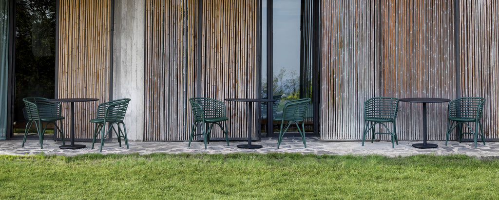 Green chairs and black tables arranged outside against a wooden wall.