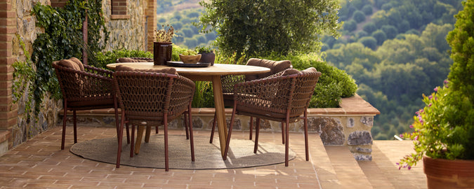 Brown chairs surrounding a round table on a scenic terrace with greenery.
