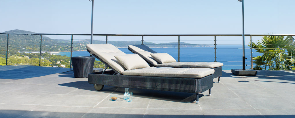 Two modern grey and black lounge chairs on a terrace overlooking the ocean.