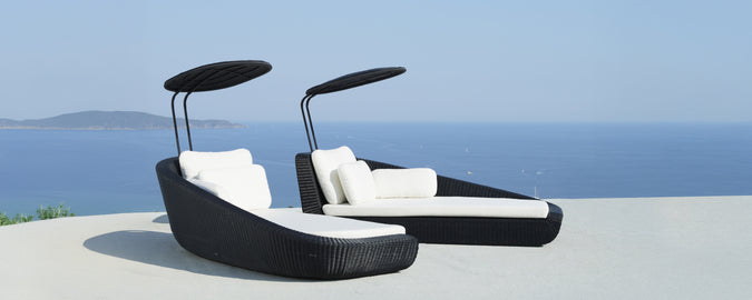 Modern black lounge chairs with white cushions overlooking the sea.