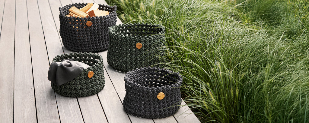 Collection of black woven baskets arranged on a wooden deck with greenery in the background.