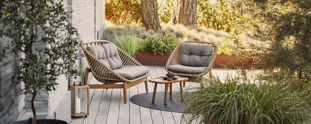 Modern grey lounge chairs with cushions and a small side table in an outdoor setting.