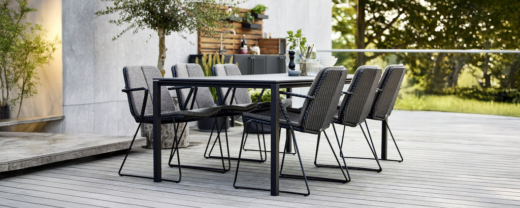 Black dining table with grey chairs in a modern outdoor setting.
