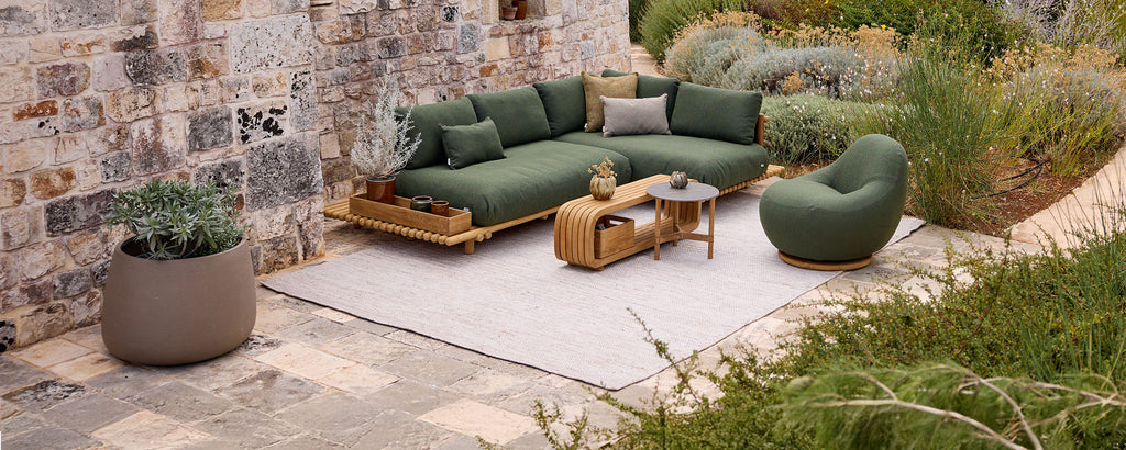 Modern outdoor lounge setting with green sectional sofa, chair, wooden coffee table, and grey rug.