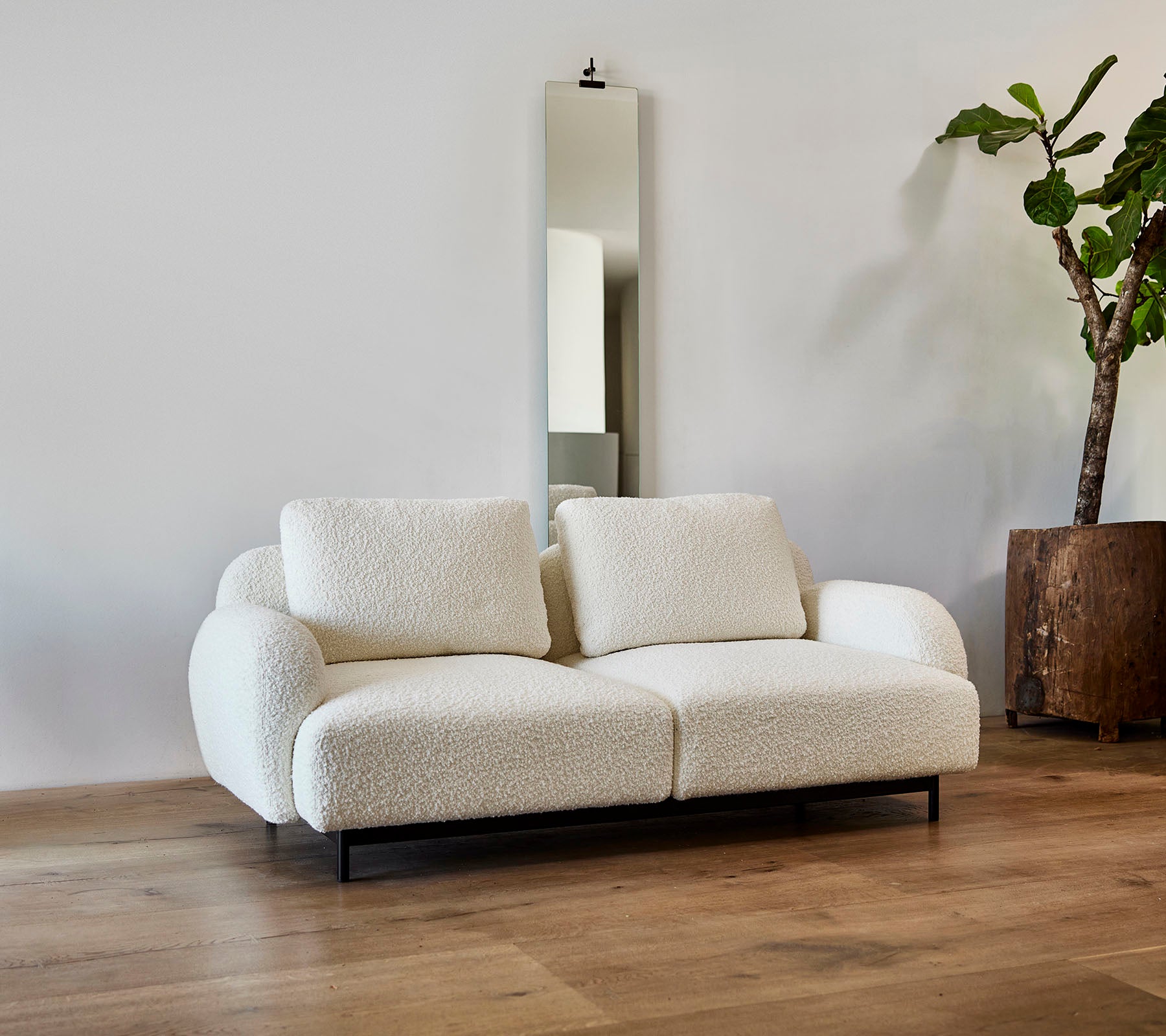A stylish white sofa featuring plush cushions, paired with a large mirror and a potted plant in a modern setting.