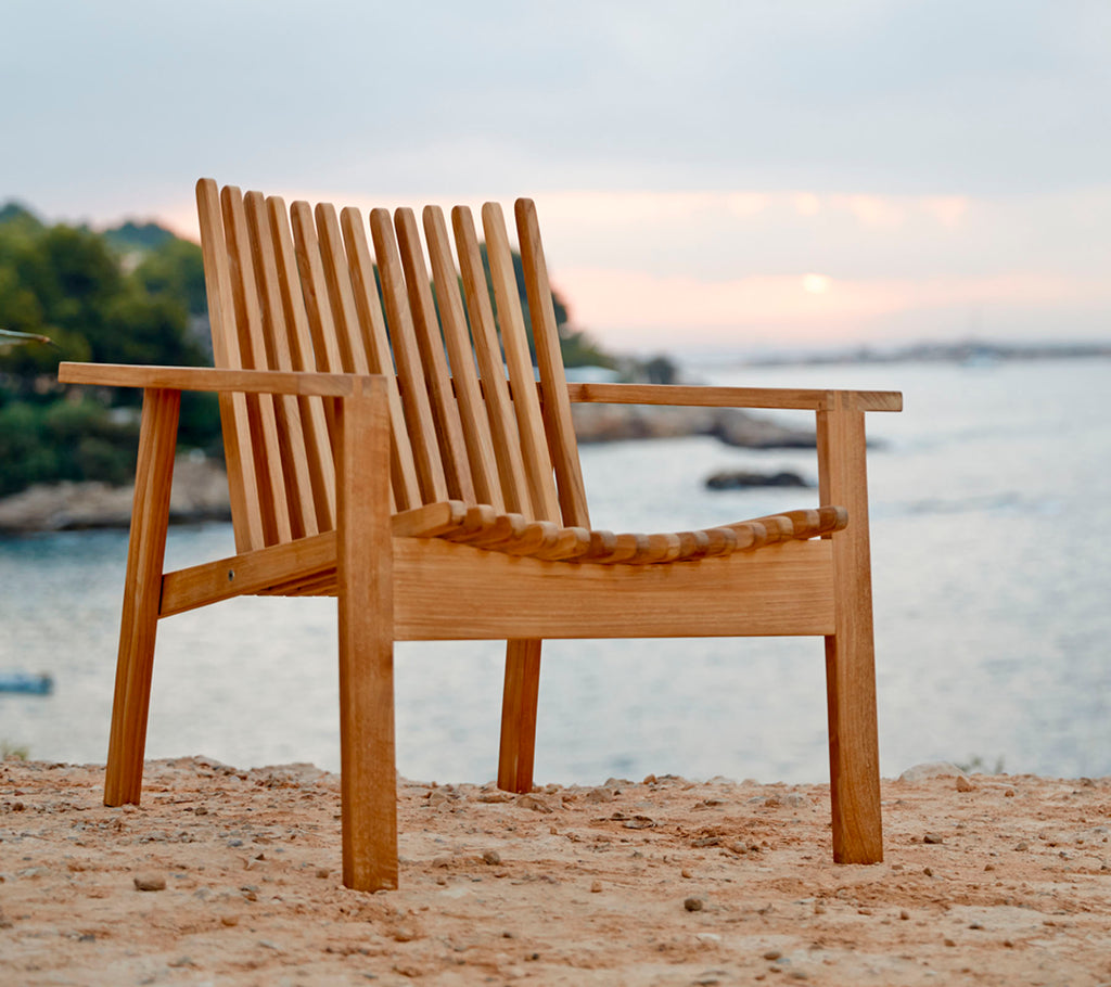 A wooden chair with slatted back and seat, positioned near water, showcasing a natural and serene setting.