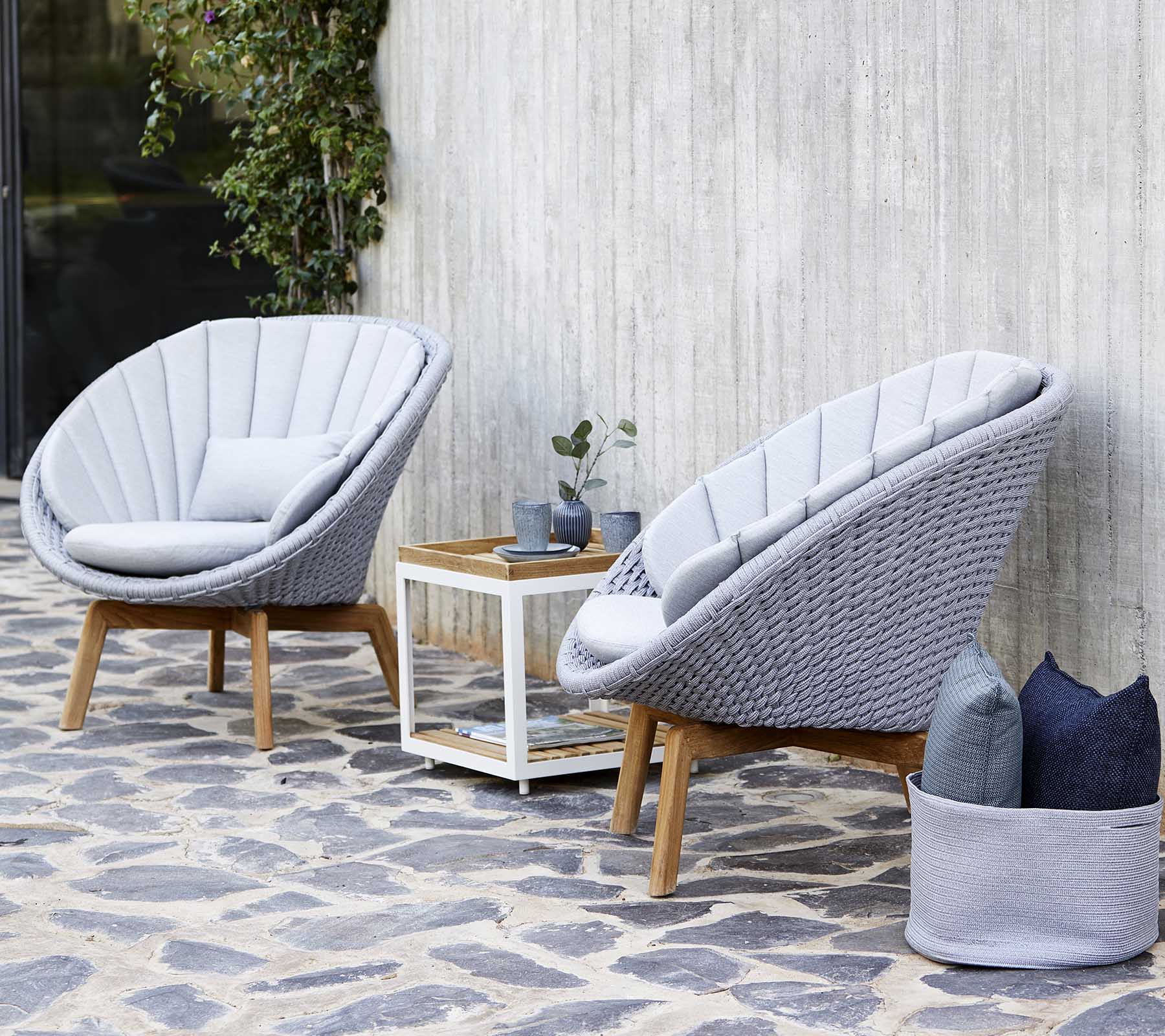 Two stylish gray lounge chairs with a wooden frame are positioned beside a white side table, adorned with a small plant and decorative pillows.