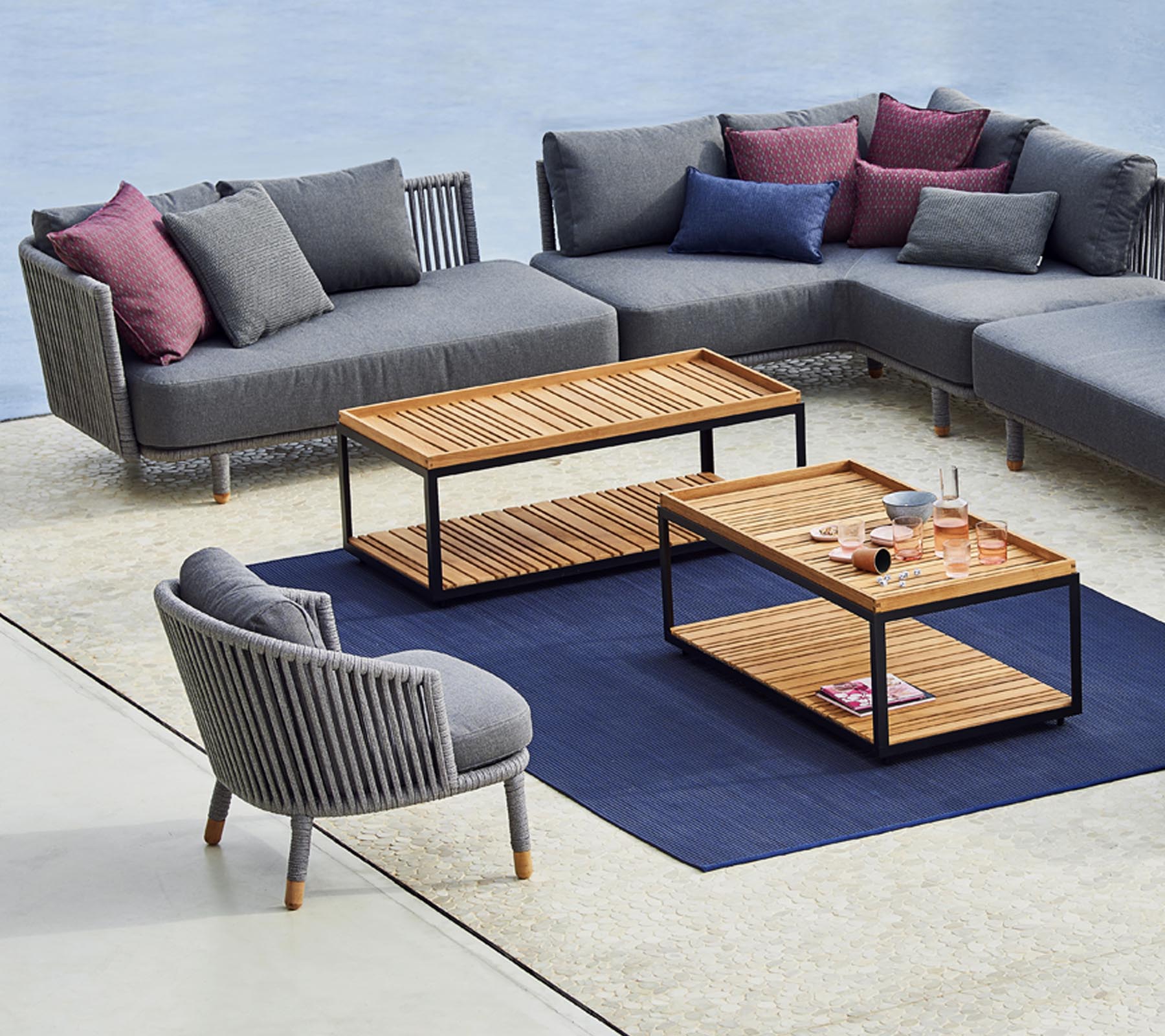 Modern seating arrangement featuring a grey sectional sofa, a stylish round chair, and wooden coffee tables with a blue rug underneath.