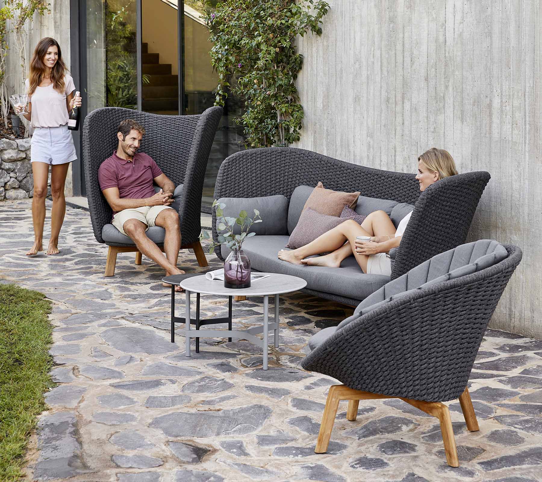 Stylish outdoor seating arrangement featuring a curved sofa and chairs, with a small table, surrounded by greenery.