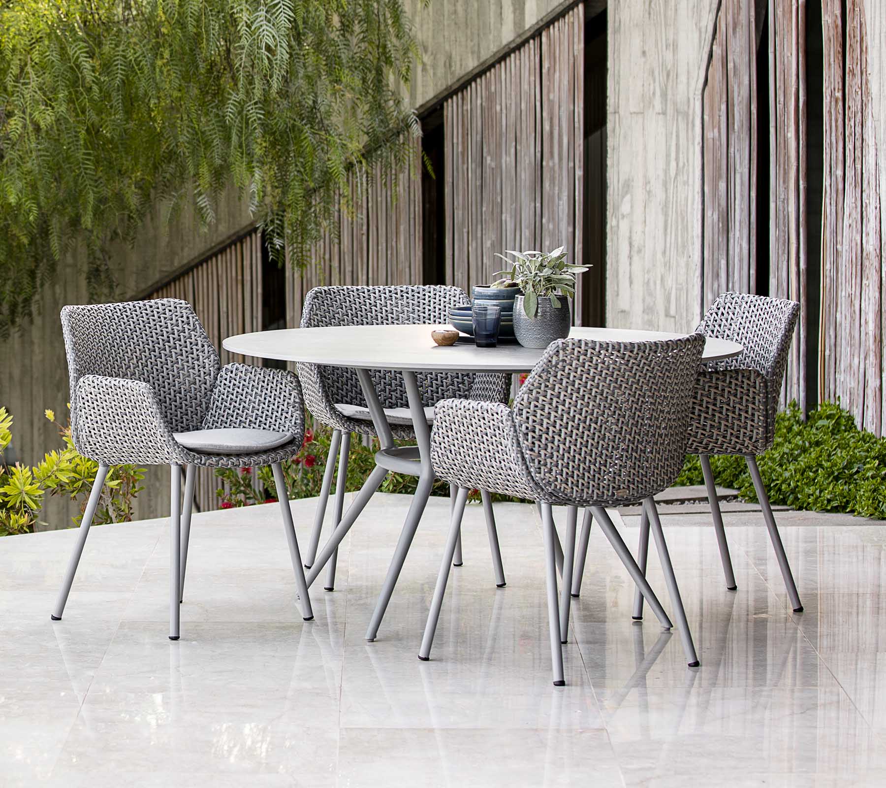 Contemporary outdoor dining table set with woven chairs, styled with plants and table decor, featuring a modern aesthetic.