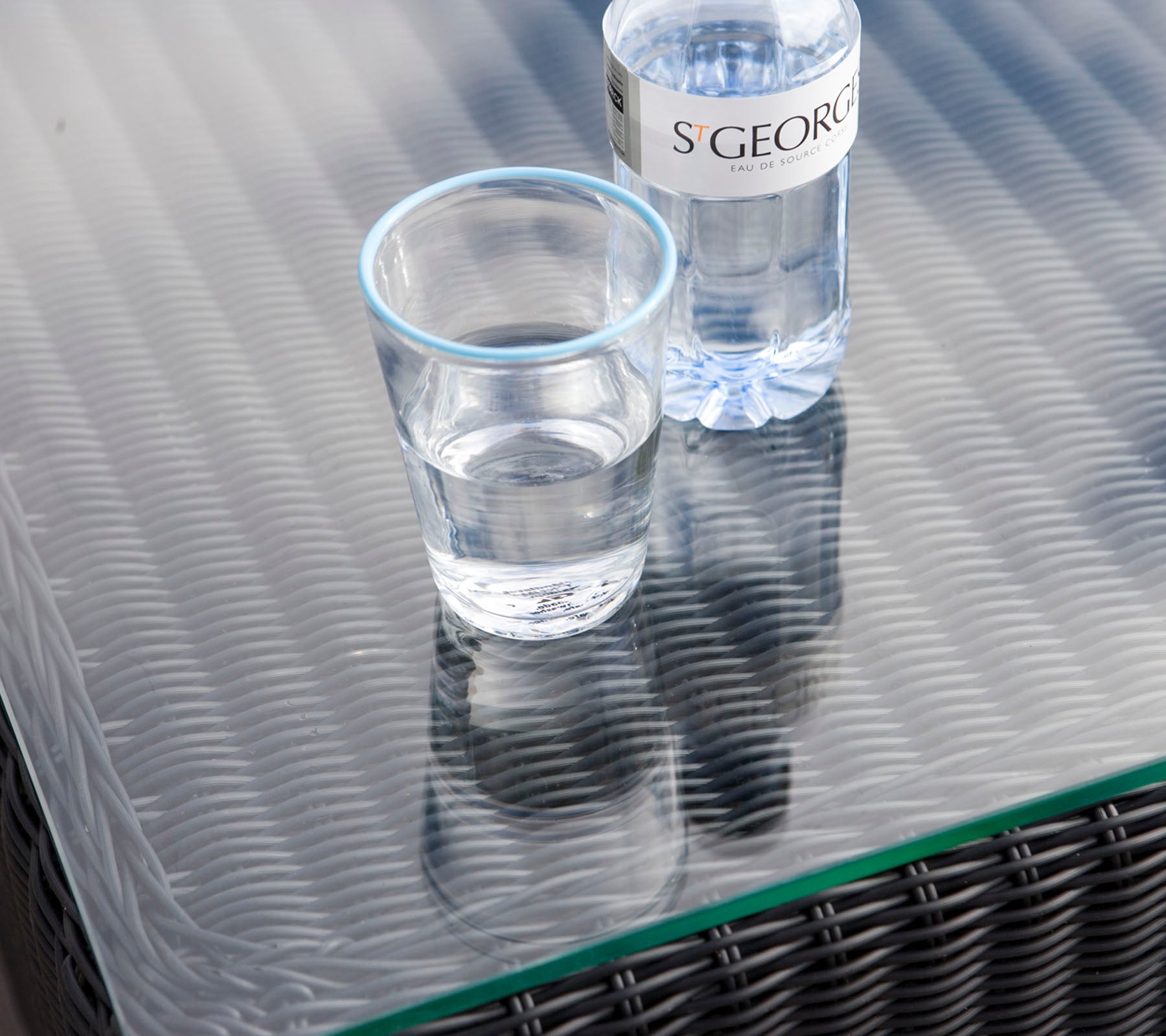 A clear glass with water next to a water bottle on a textured table surface.
