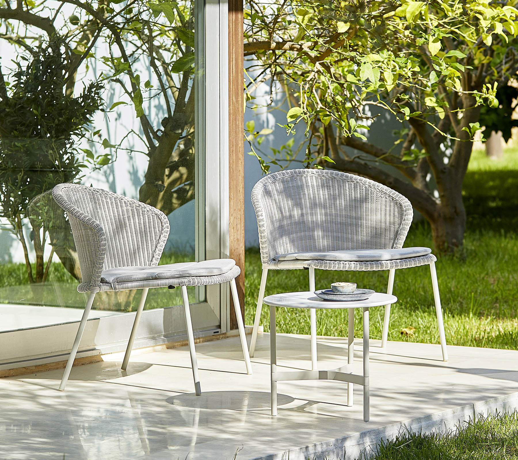 Two stylish chairs and a small table in a serene setting with greenery, perfect for relaxation and outdoor gatherings.