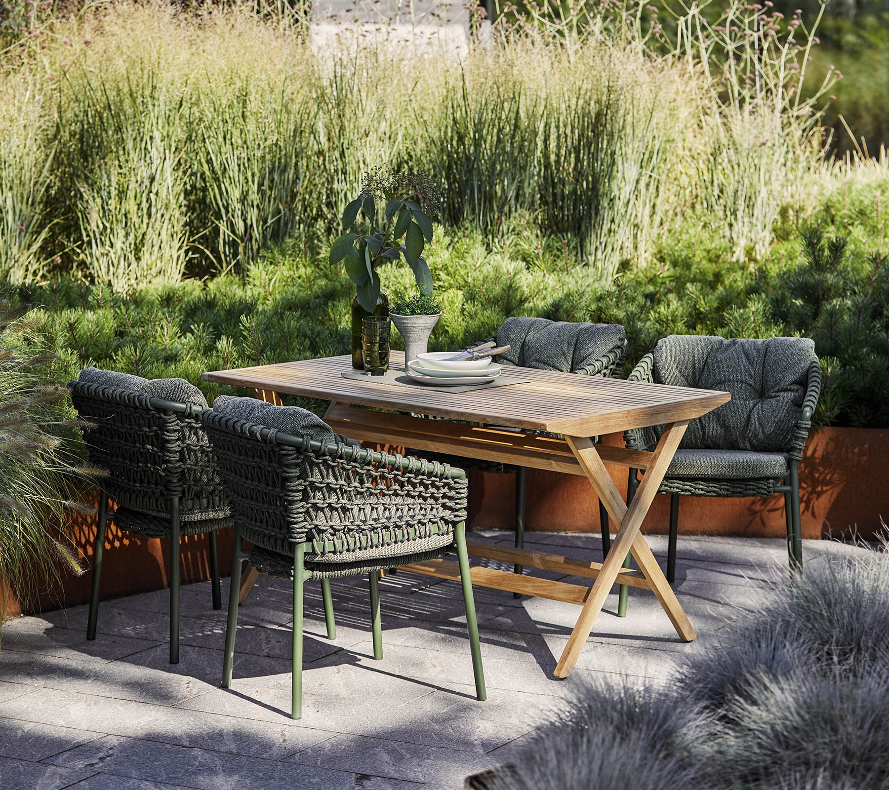 A stylish outdoor dining set featuring a wooden table and four woven chairs surrounded by lush greenery and decorative plants.
