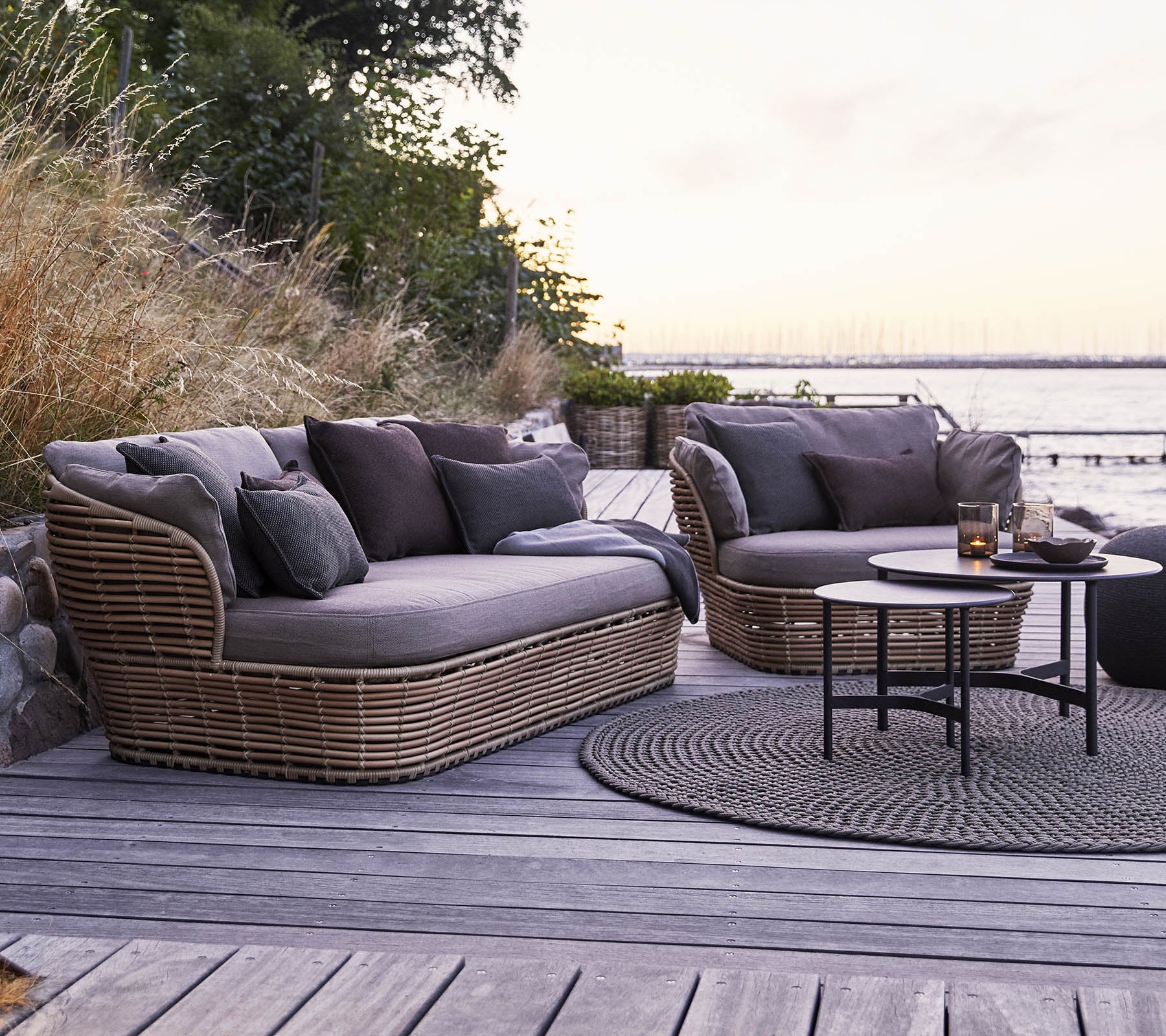 Stylish outdoor seating area featuring two plush, curved sofas with dark cushions and a round coffee table on a wooden surface.