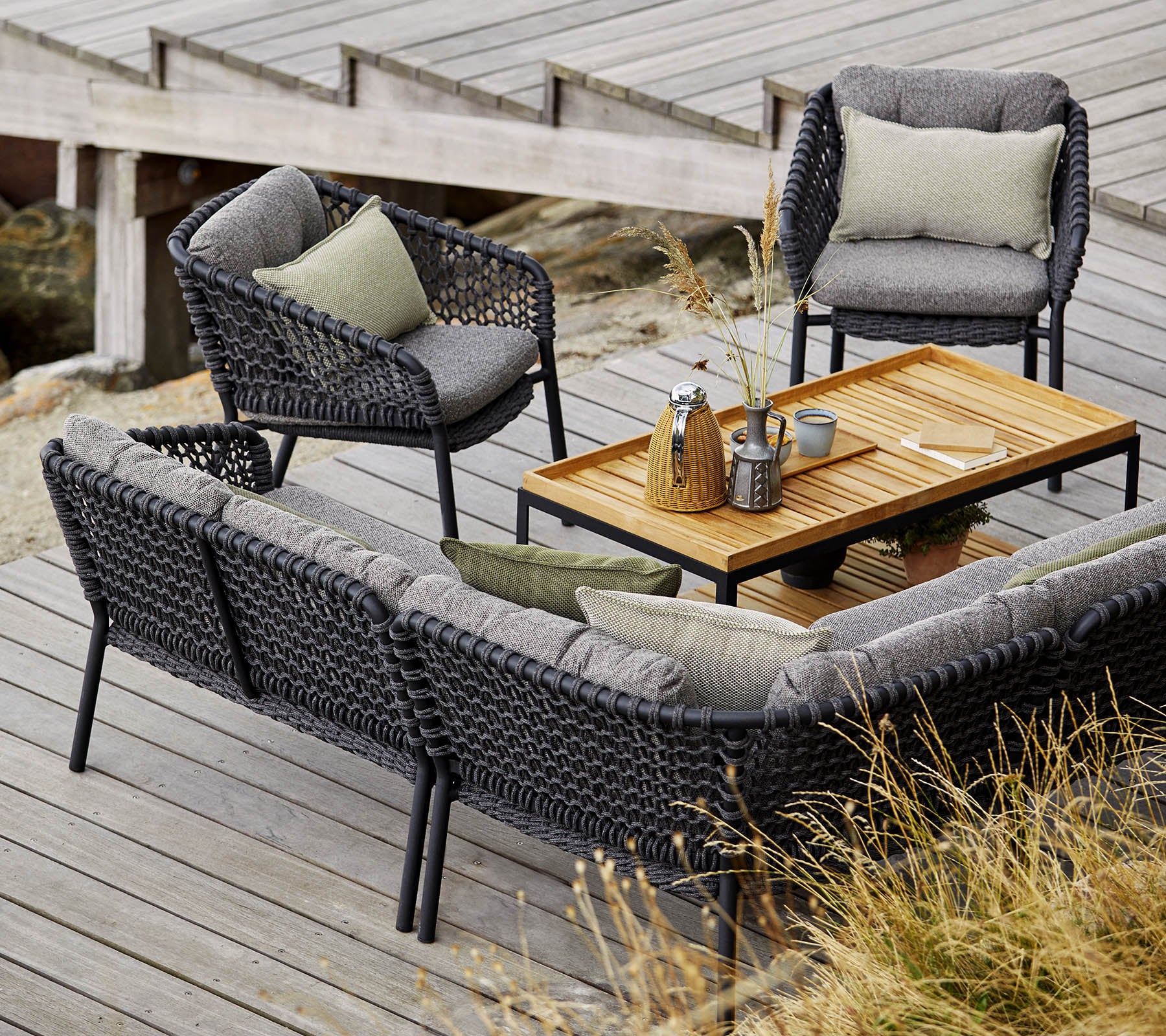 Stylish outdoor seating set featuring a cozy sofa, two chairs, and a wooden coffee table, accented with soft cushions and decor items.
