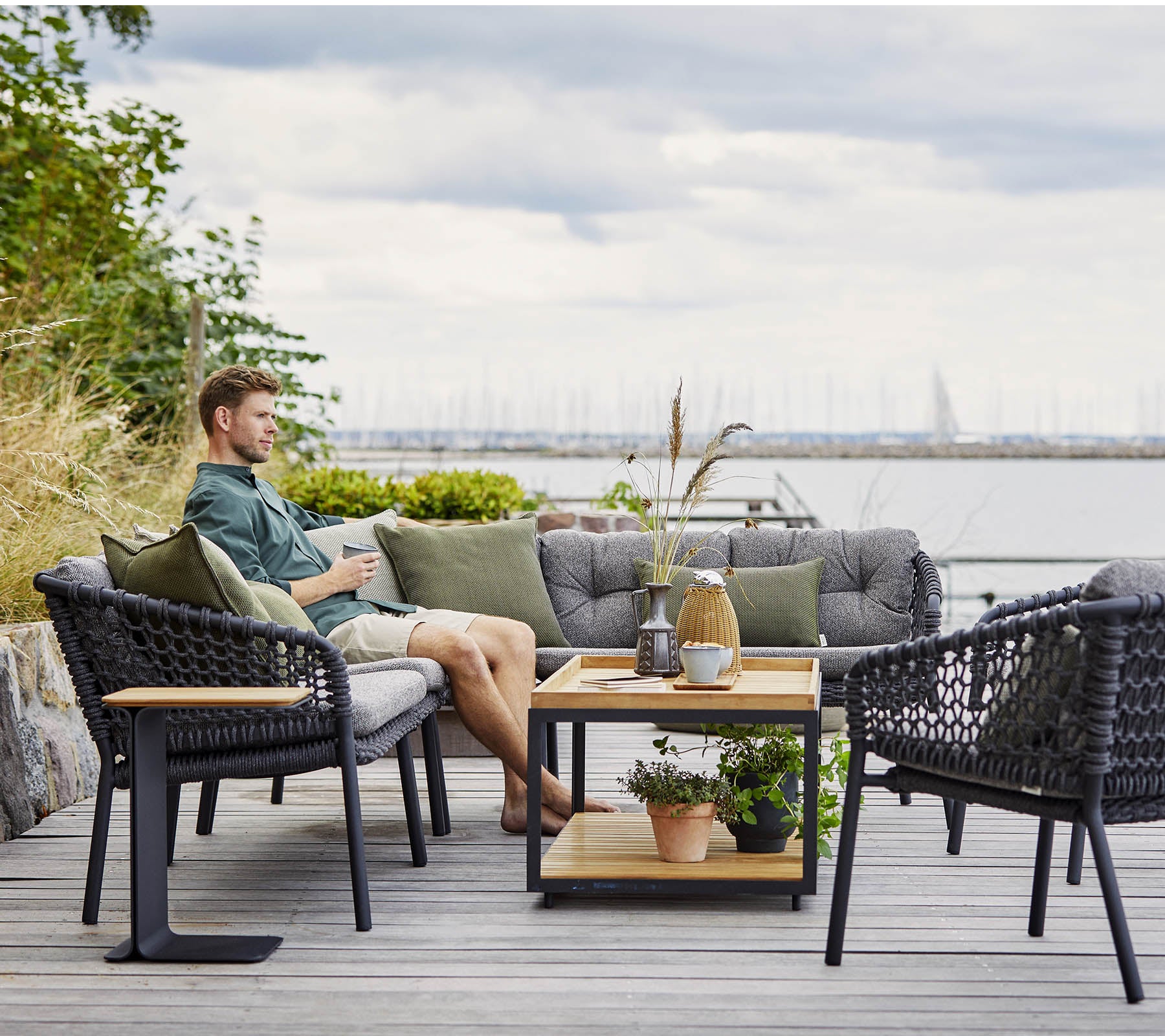A comfortable seating area with a man relaxing, featuring stylish wicker chairs and a wooden coffee table adorned with plants and decorative items.