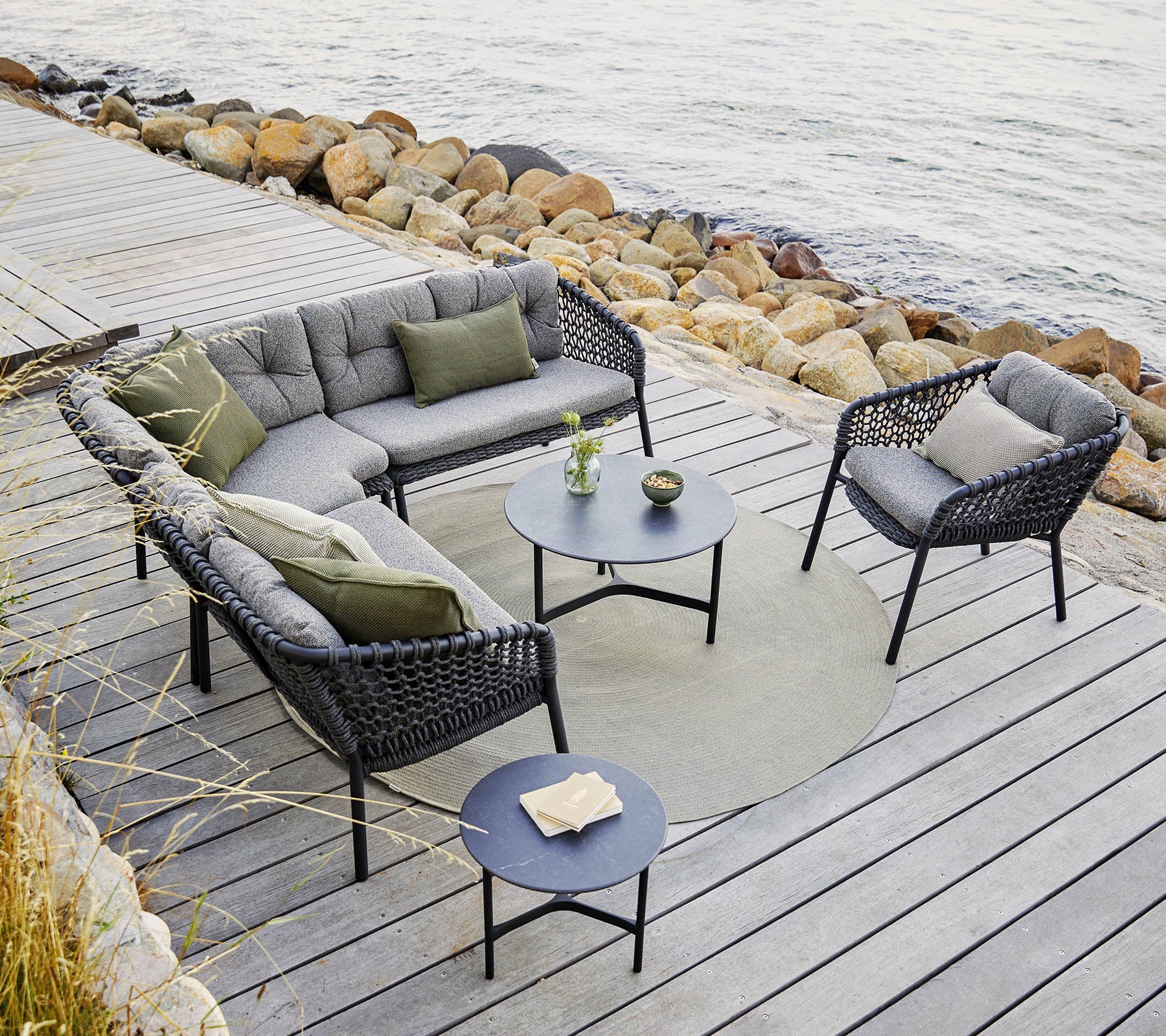 A stylish outdoor seating arrangement featuring a sectional sofa and chairs with gray cushions, a round table, and decorative accents.