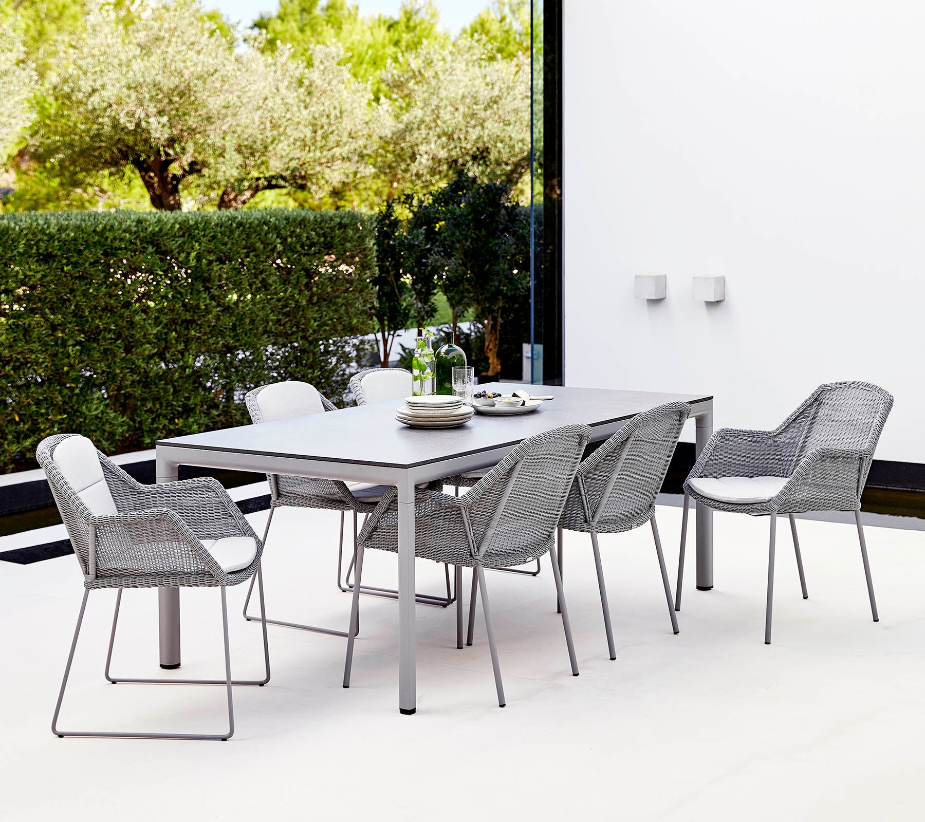 A modern dining set featuring a rectangular table and six stylish woven chairs, surrounded by greenery.