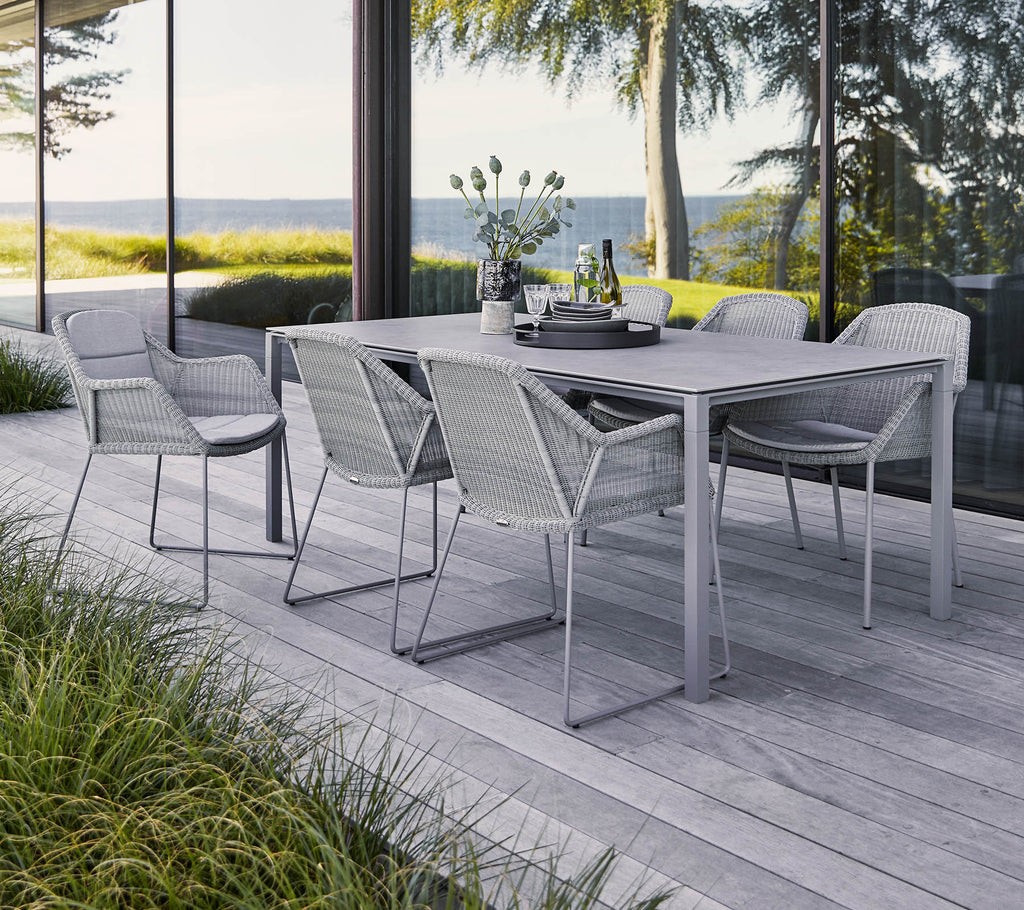 A stylish outdoor dining set featuring a rectangular table and six woven chairs, surrounded by greenery and a scenic view.
