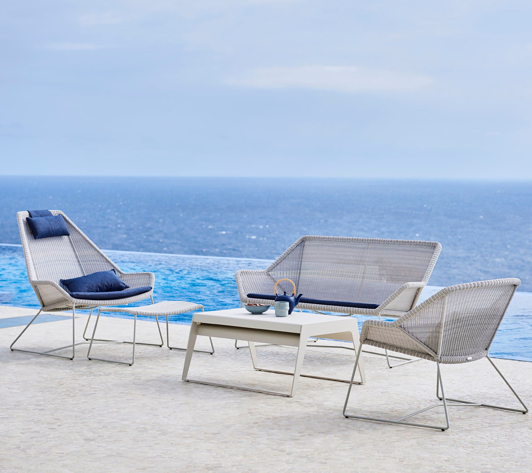 Modern outdoor furniture set featuring stylish chairs and a table, set against a backdrop of water and sky.