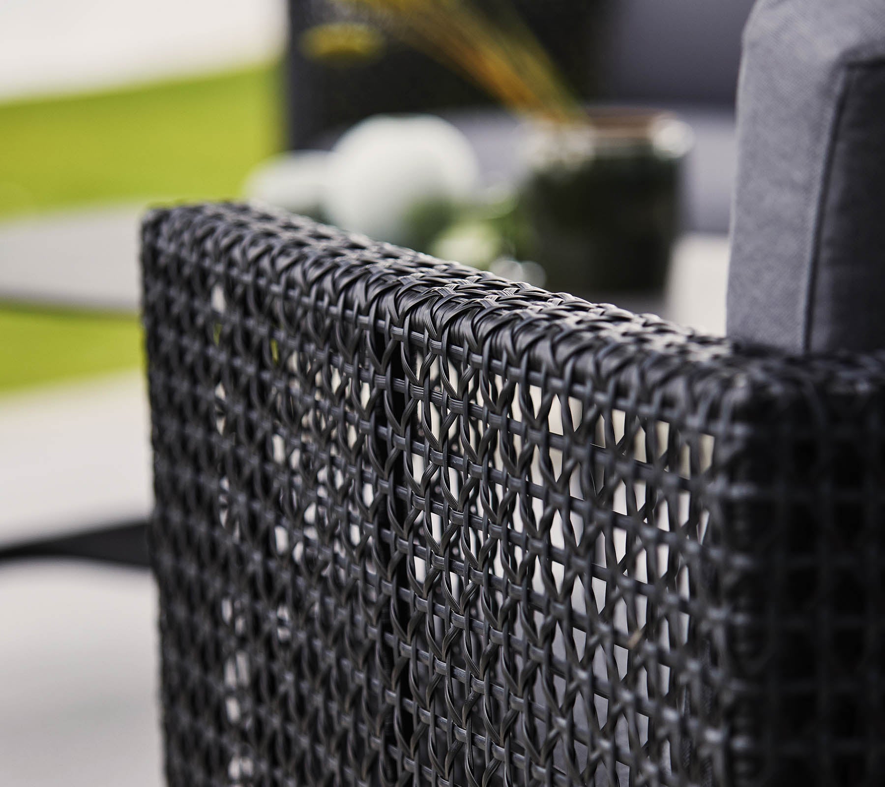 Woven black chair back with a soft cushion, featuring blurred decorative elements in the background.