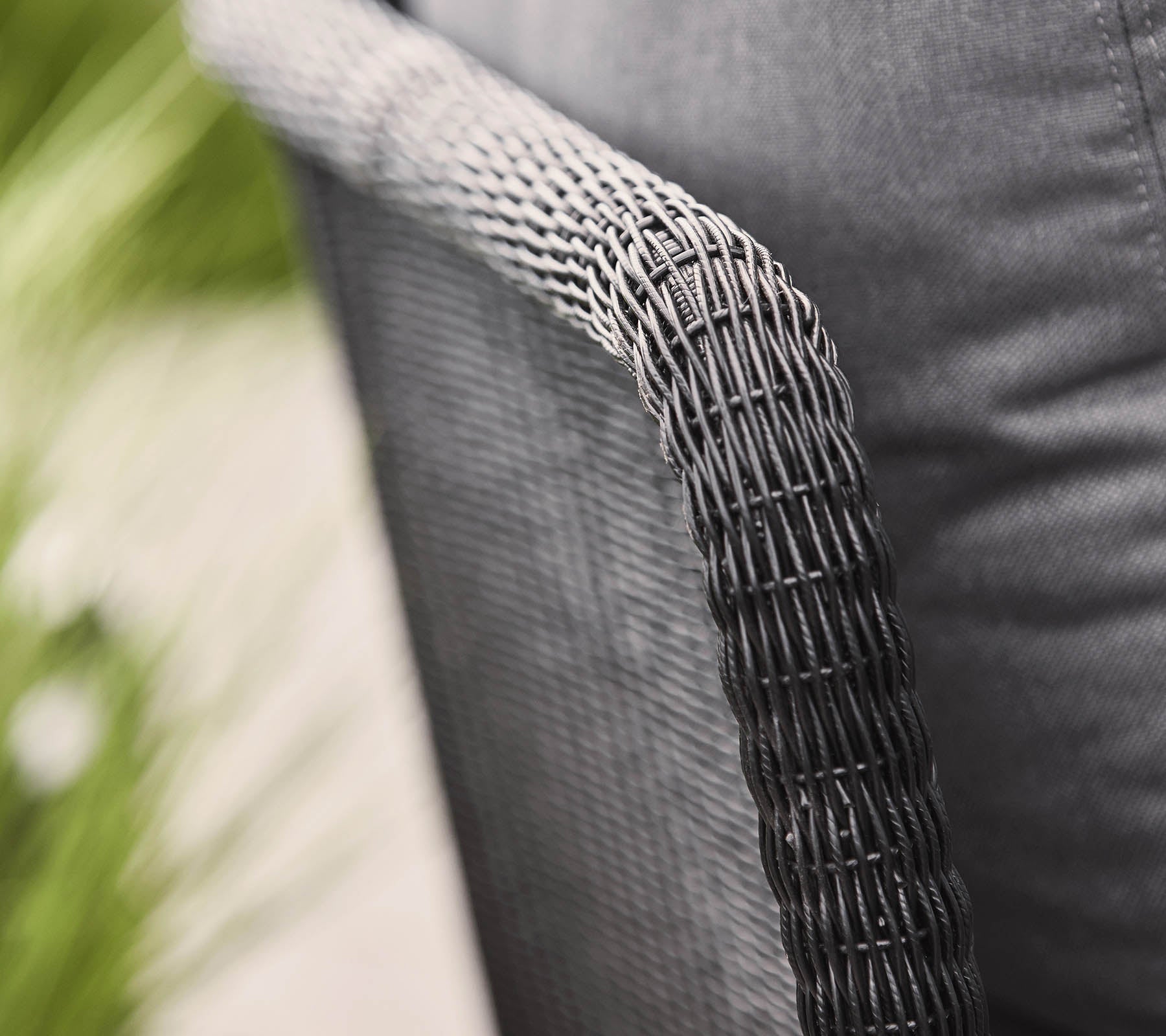 Close-up of a woven chair arm with a textured black finish, showcasing a modern design and cozy fabric seat.