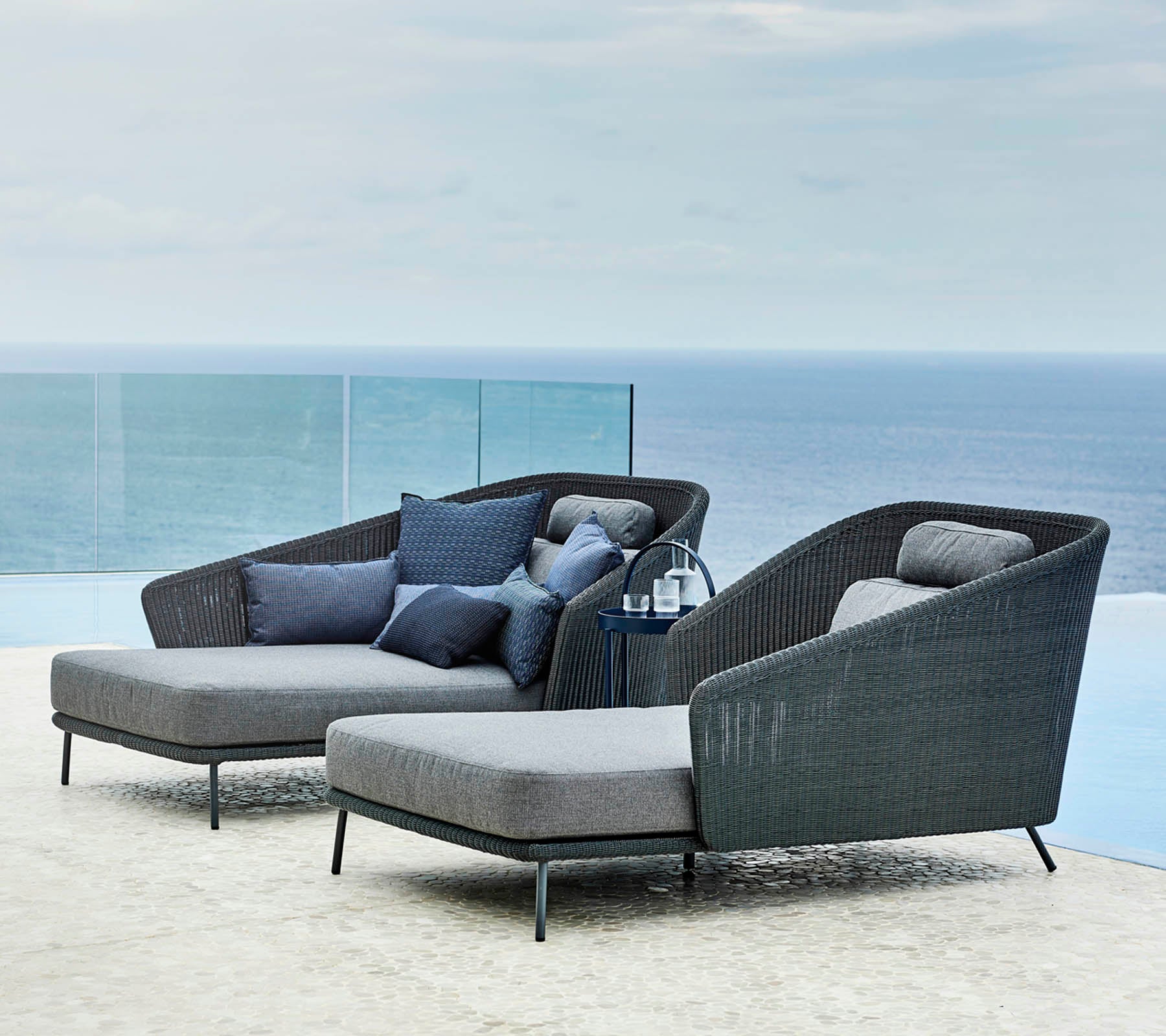 Two stylish lounge chairs with cushions and a small side table, overlooking a serene ocean view.