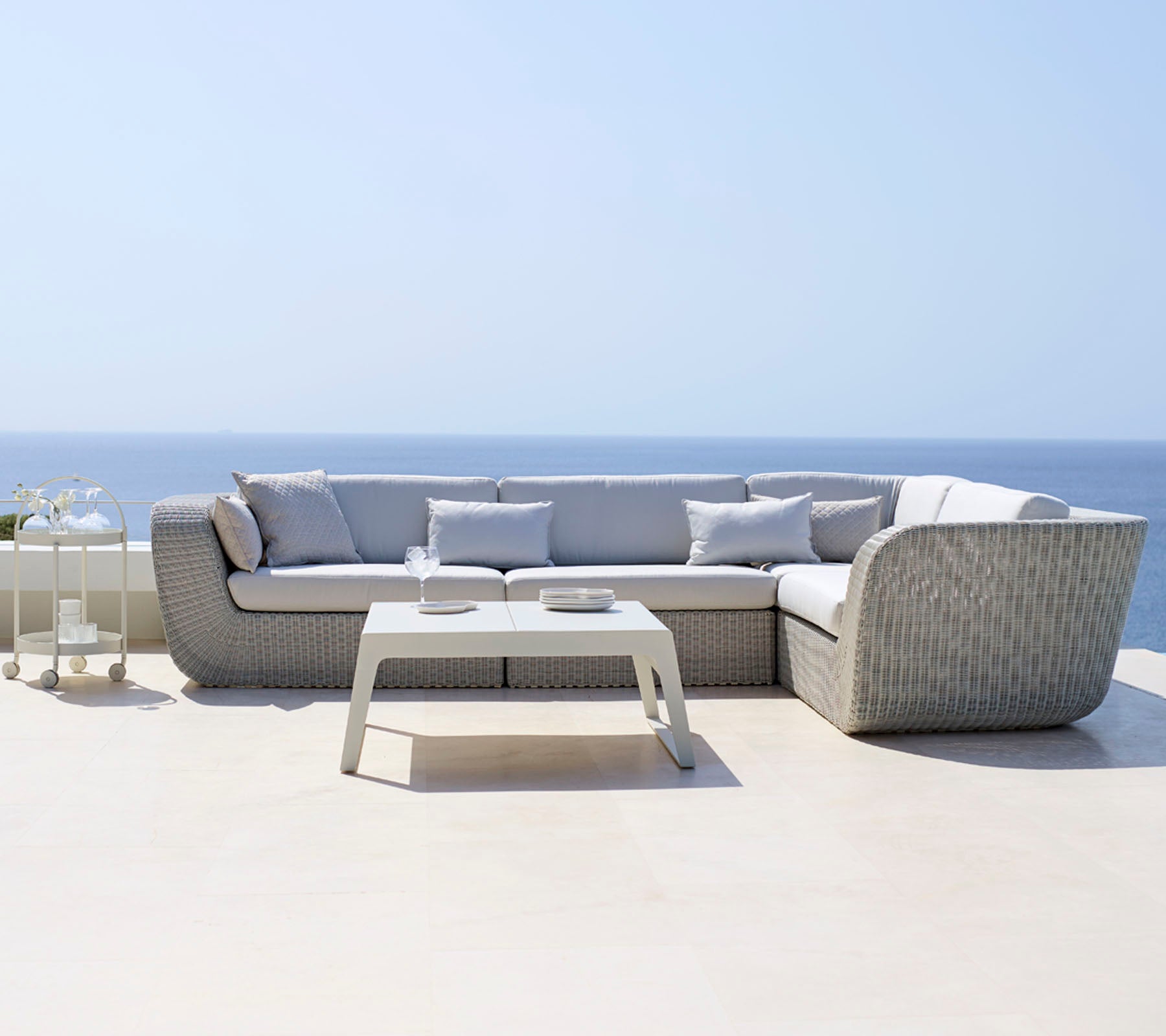 Modern sectional sofa with light gray cushions paired with a sleek white coffee table, situated against a serene ocean backdrop.