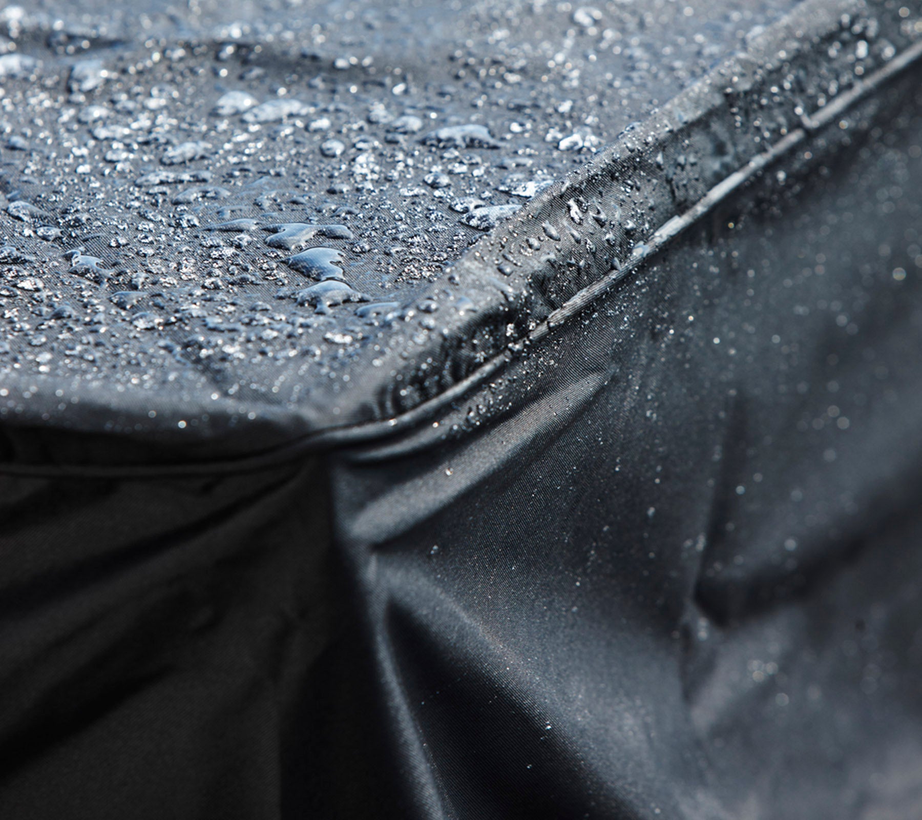 Close-up of a black waterproof cover with droplets of water on its surface, showcasing its protective design.