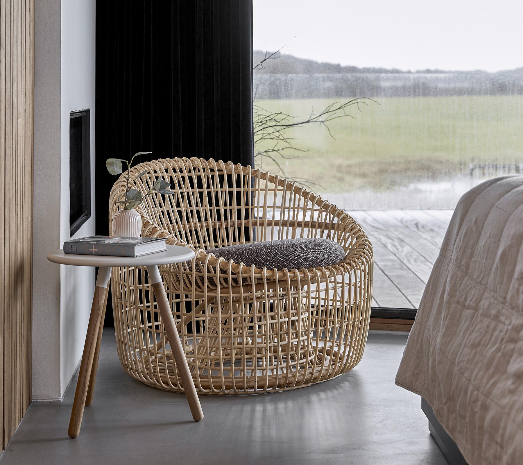 A stylish woven chair paired with a small side table, set in a serene environment with large windows letting in natural light.