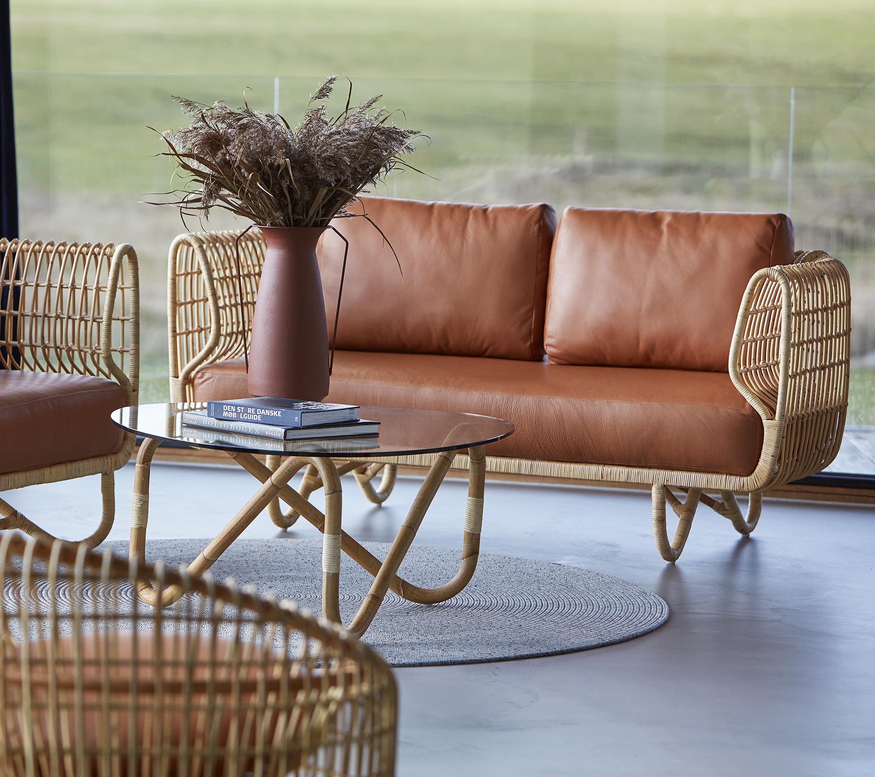 A stylish seating area featuring a brown leather sofa, a round coffee table, and decorative elements like a vase with dried flowers.