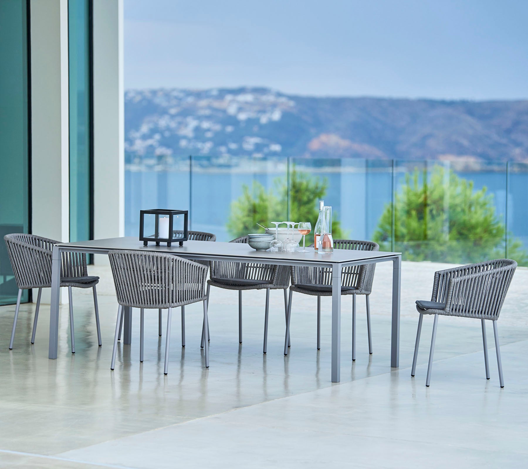 Elegant outdoor dining set featuring a rectangular table and stylish woven chairs with scenic views in the background.
