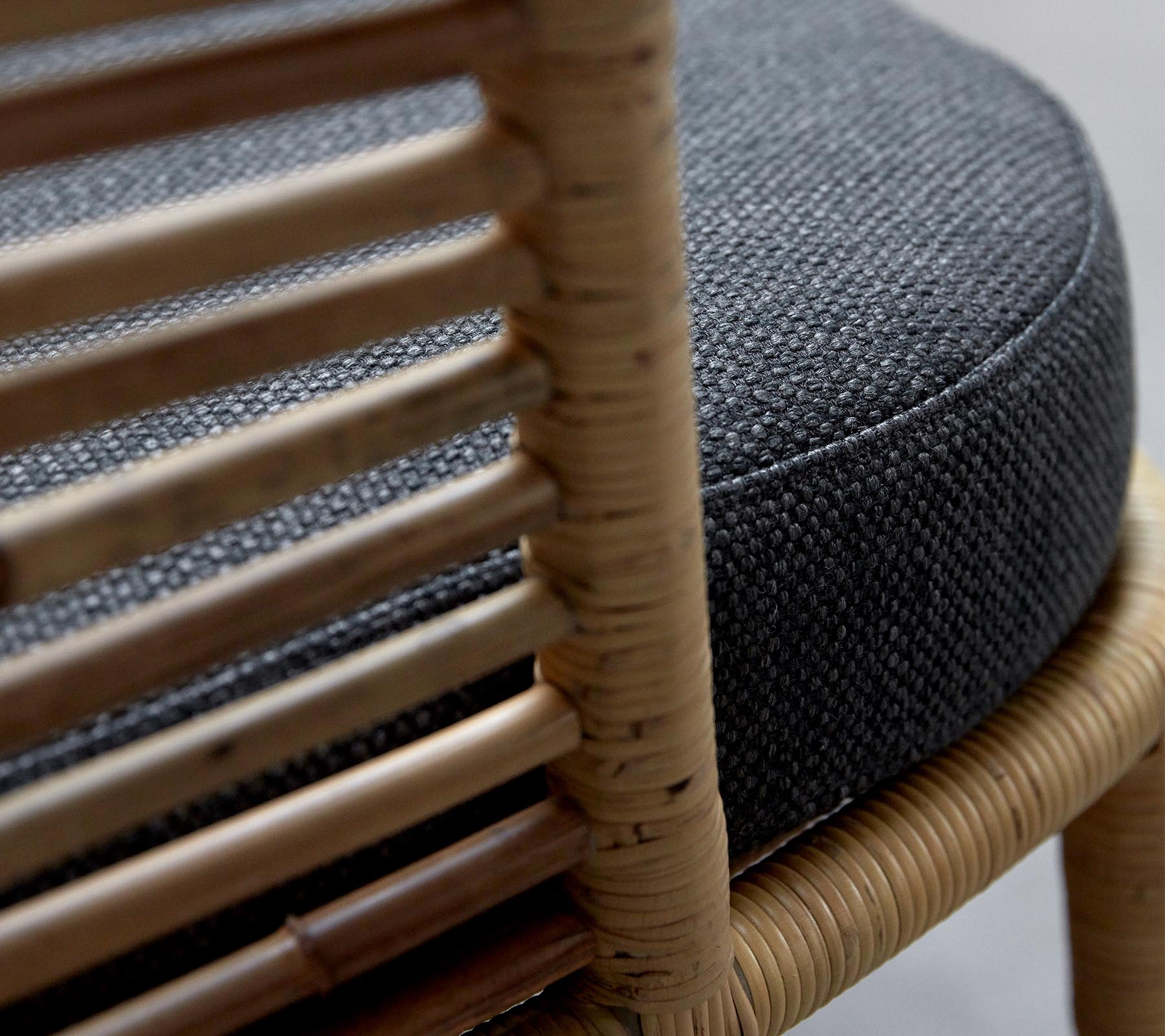 Close-up of a woven chair with a round, dark gray cushion and natural wooden frame showcasing intricate detailing.