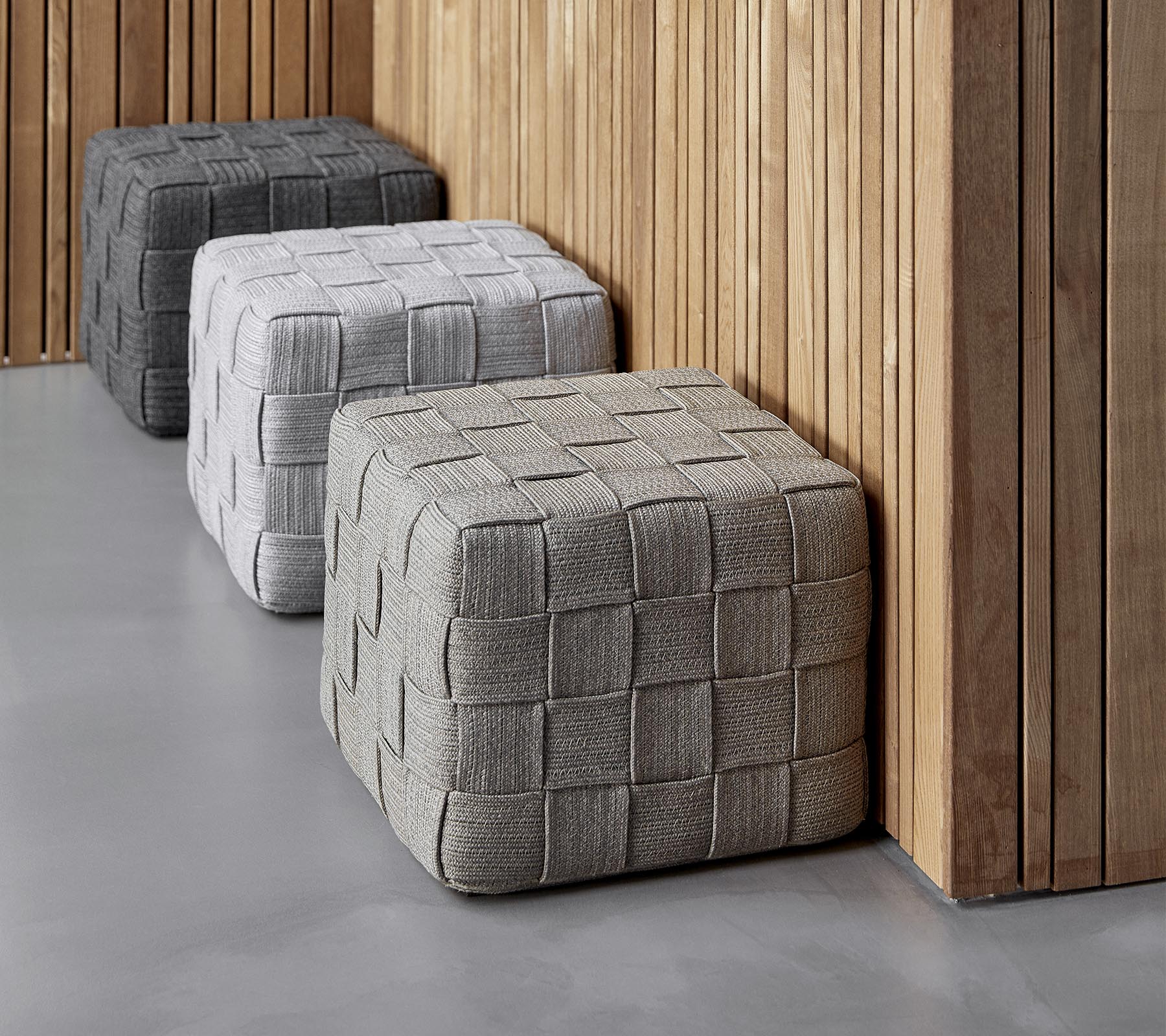 Three textured, square ottomans in varying shades of gray are positioned against a wooden wall, adding a modern touch to the setting.