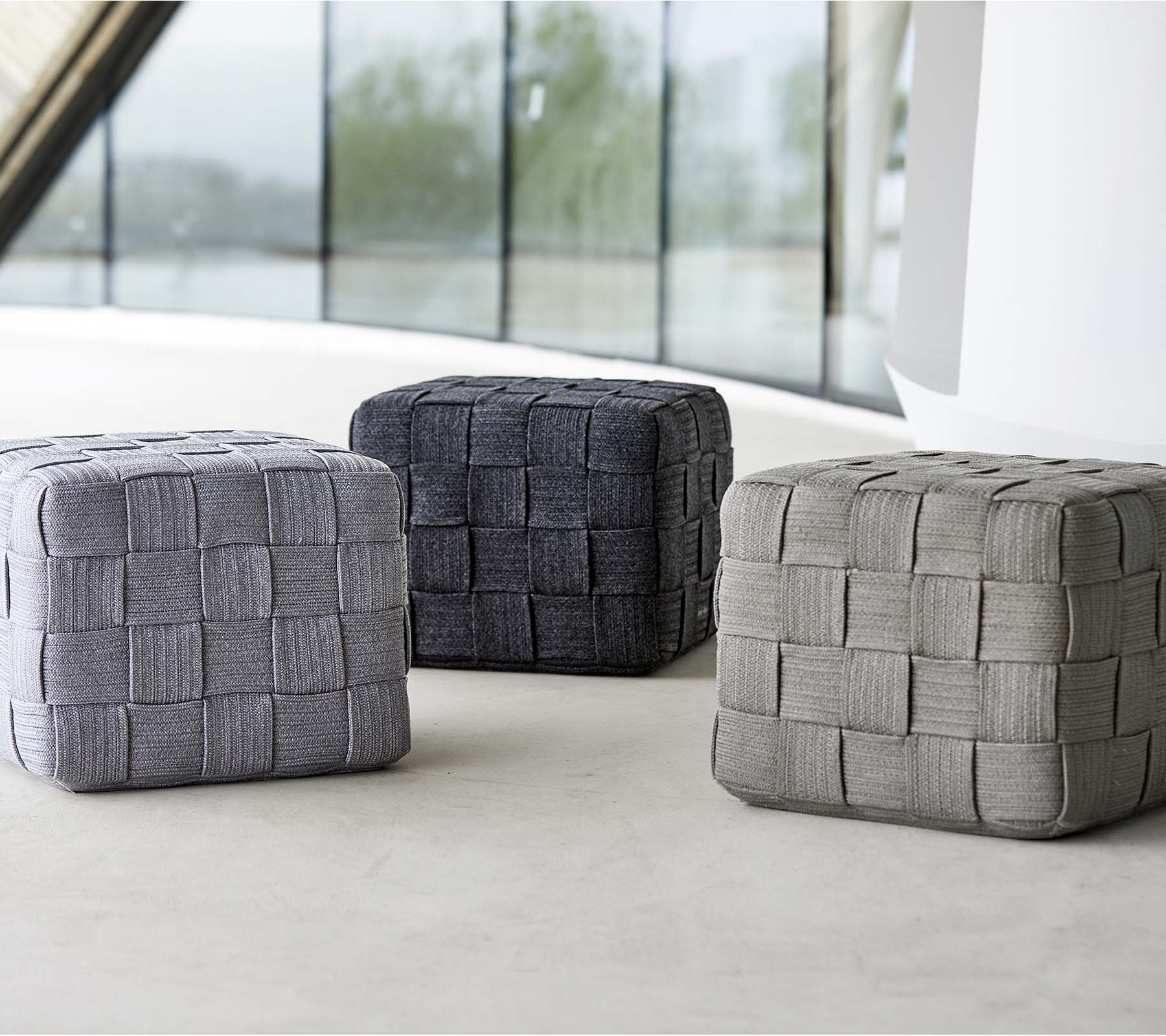 Three woven poufs in varying shades of gray, featuring a textured design, arranged on a light surface. Ideal for seating or decor.