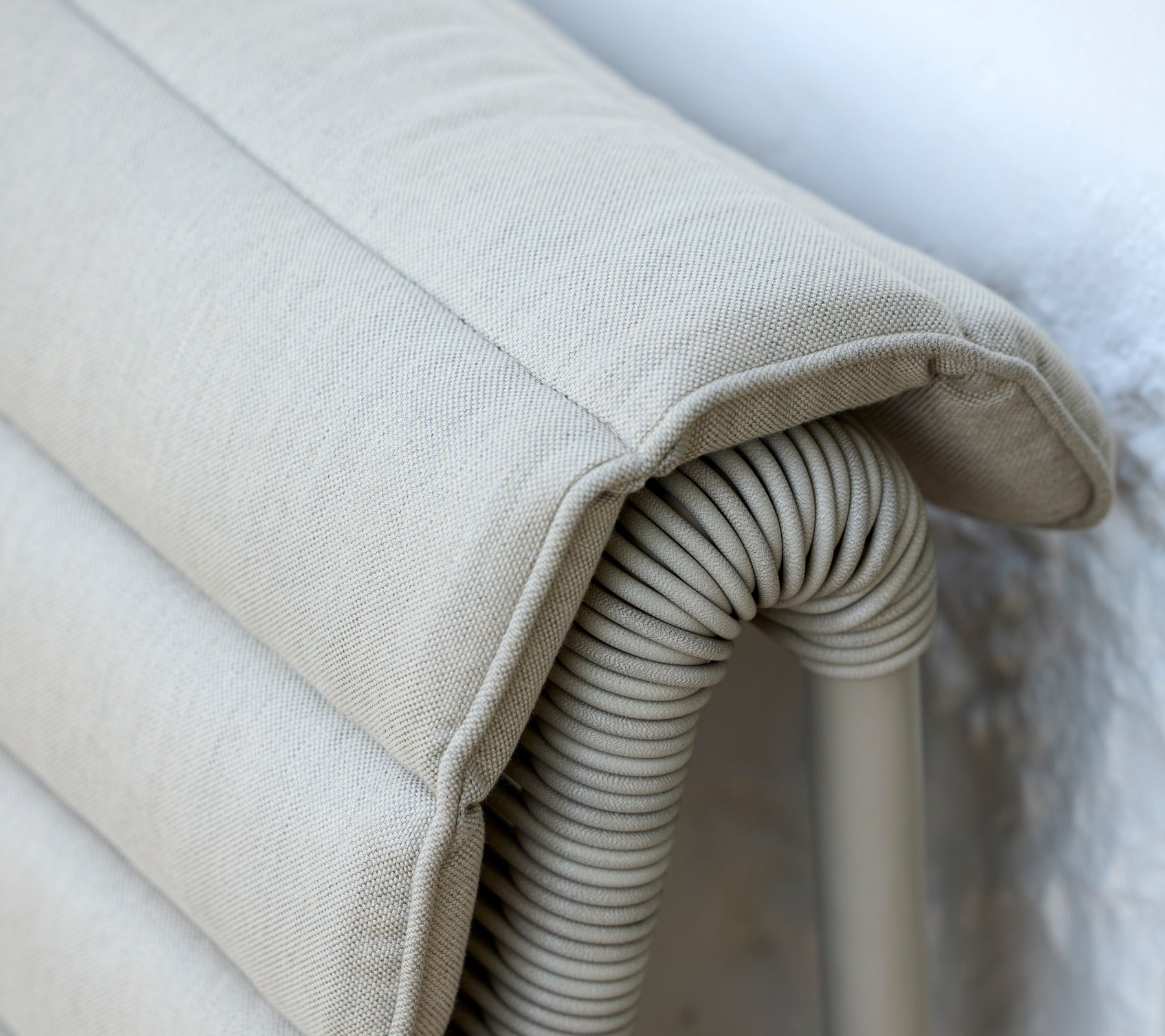 Beige cushion with a ribbed texture resting against a light wall.