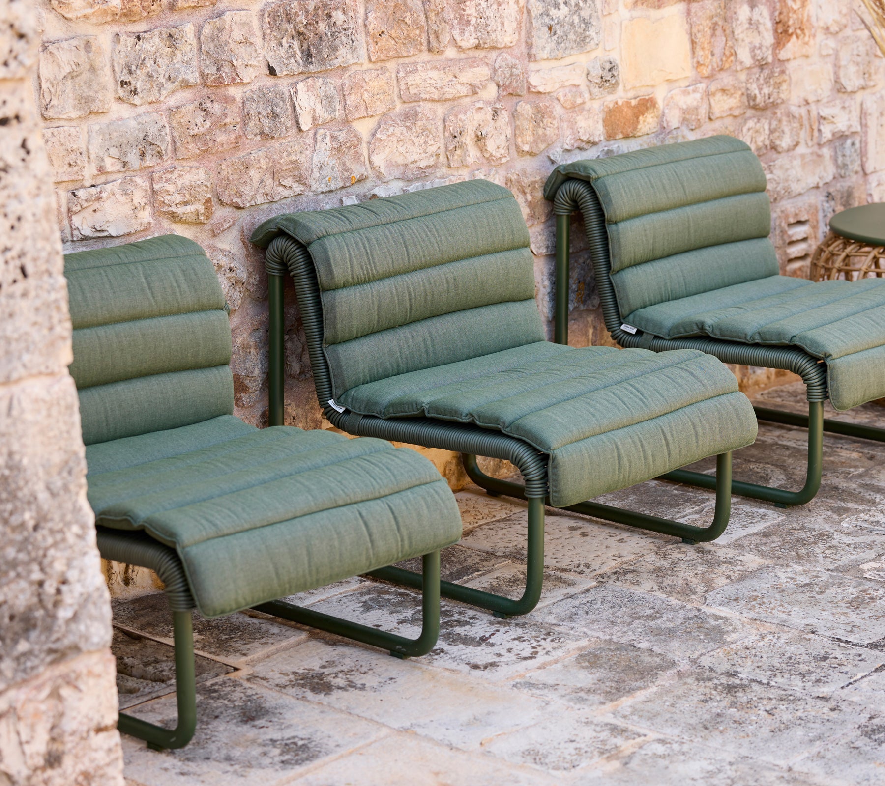 Green lounge chairs arranged against a stone wall.
