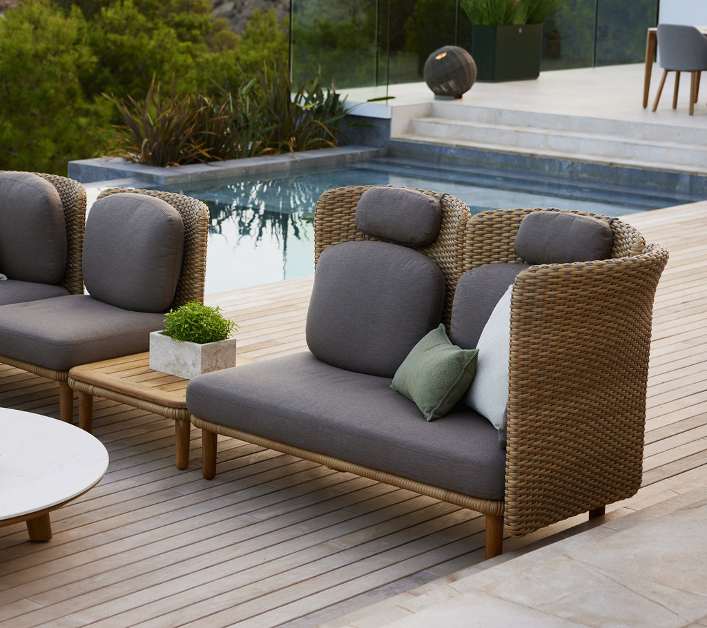 Stylish sofa with high backrest and arch armrests, featuring gray cushions and a mix of decorative pillows on a wooden deck.